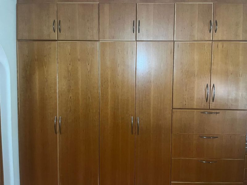 A bedroom featuring extensive floor-to-ceiling wooden built-in cupboards with integrated storage drawers and metal hardware.