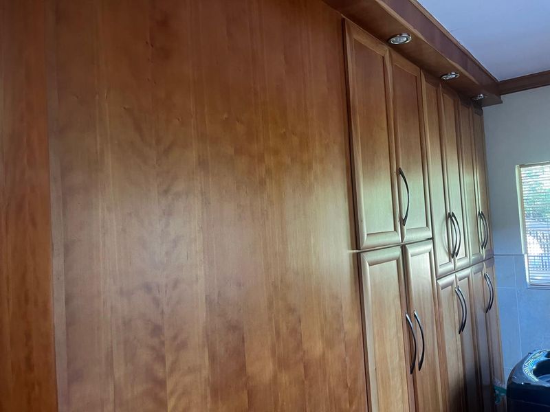 A laundry room featuring extensive built-in wooden cabinetry with integrated downlighting and a window providing natural light.