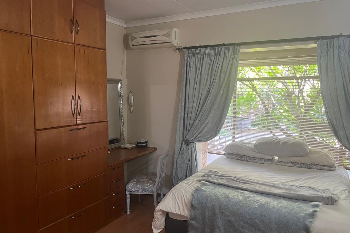 A bedroom featuring built-in wooden cupboards, laminate flooring, and a wall-mounted split-system air conditioner.