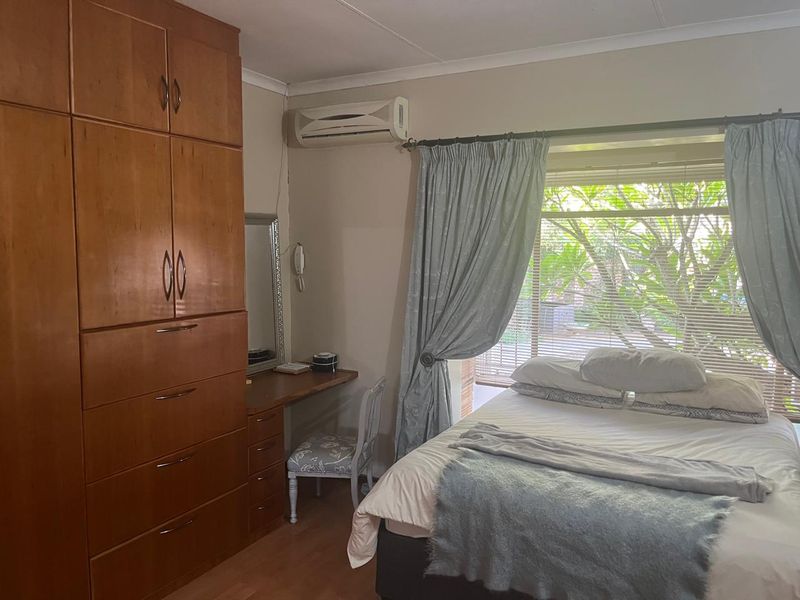 A bedroom featuring built-in wooden cupboards, laminate flooring, and a wall-mounted split-system air conditioner.