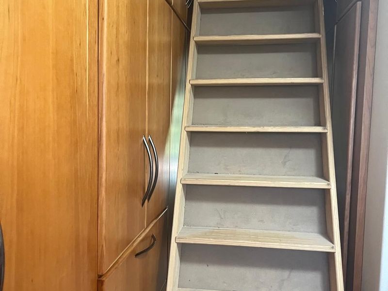 A narrow utility space featuring built-in wooden cabinetry and a fixed attic access ladder.