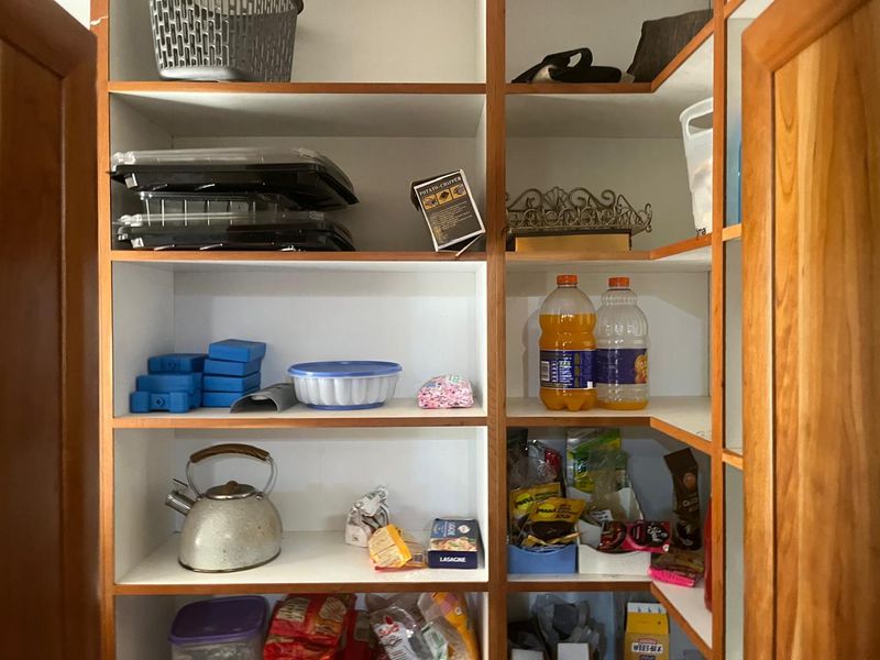 A functional pantry or scullery storage area featuring built-in shelving and timber cabinet doors.