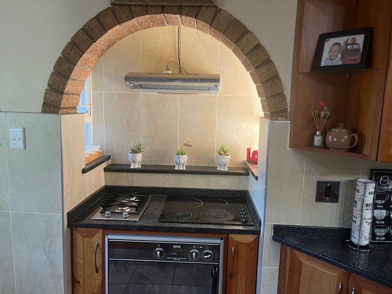 A kitchen cooking station featuring a distinctive brick archway, granite countertops, and a combination gas and electric hob with an integrated oven.