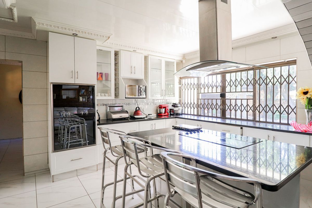 Modern kitchen featuring a central island with granite countertops, built-in oven, extractor fan, and ample white cabinetry with glass-front display sections.