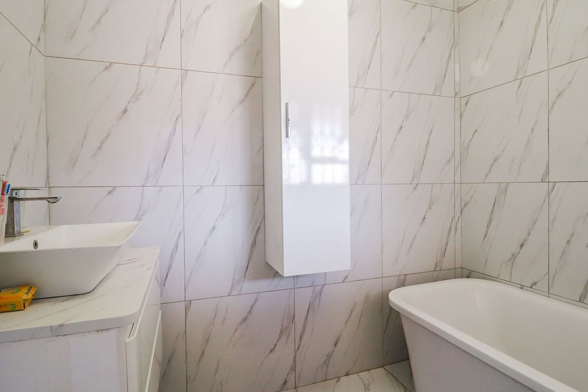 Modern bathroom featuring marble-look wall tiles, a sleek vessel sink with vanity, and a contemporary freestanding bathtub.