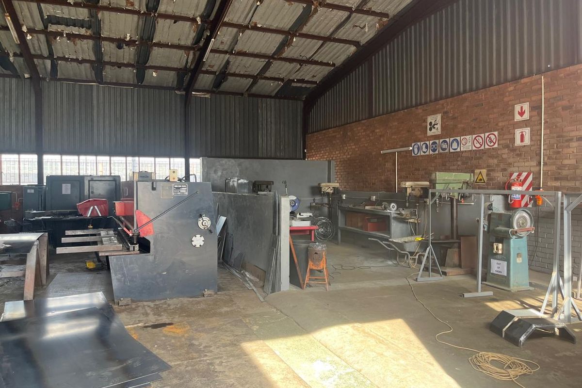 Industrial workshop space featuring exposed brick walls, high-clearance steel roof trusses, and durable concrete flooring, suitable for manufacturing or heavy-duty commercial operations.