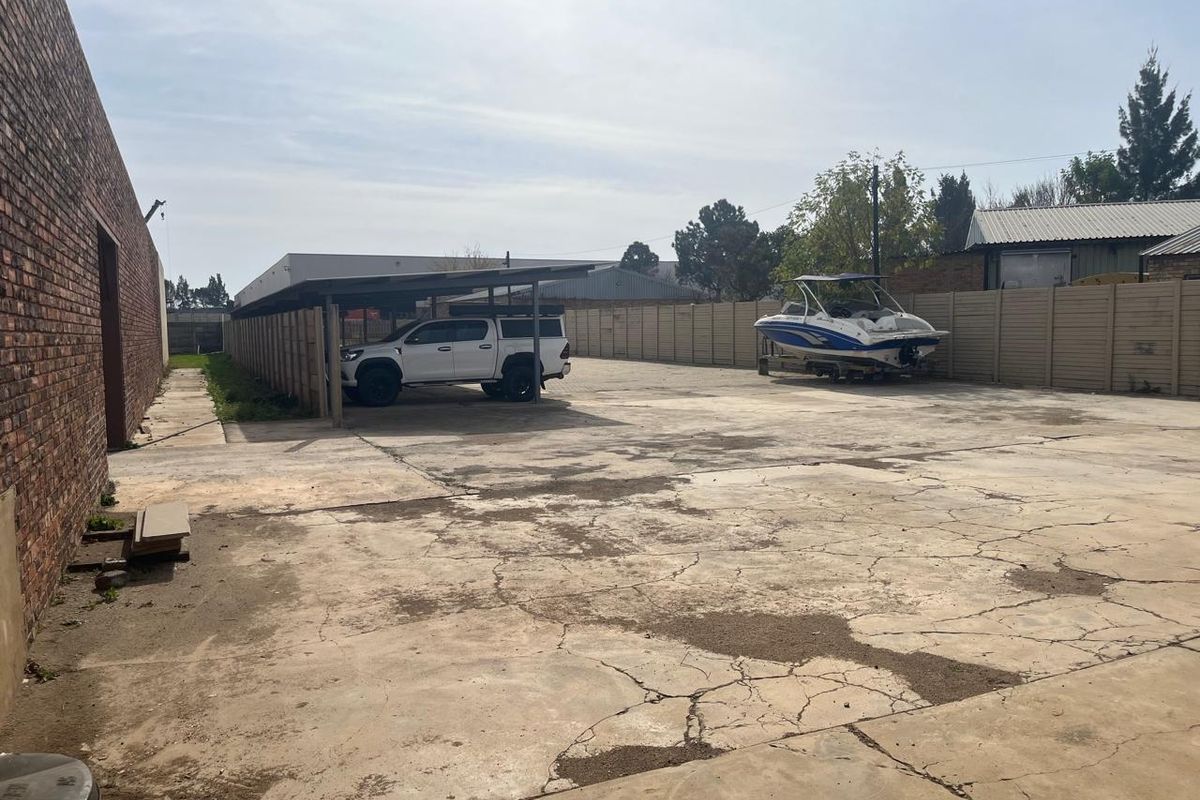 Spacious rear yard area featuring extensive concrete paving, a covered carport structure, and perimeter walling, suitable for commercial storage or parking.