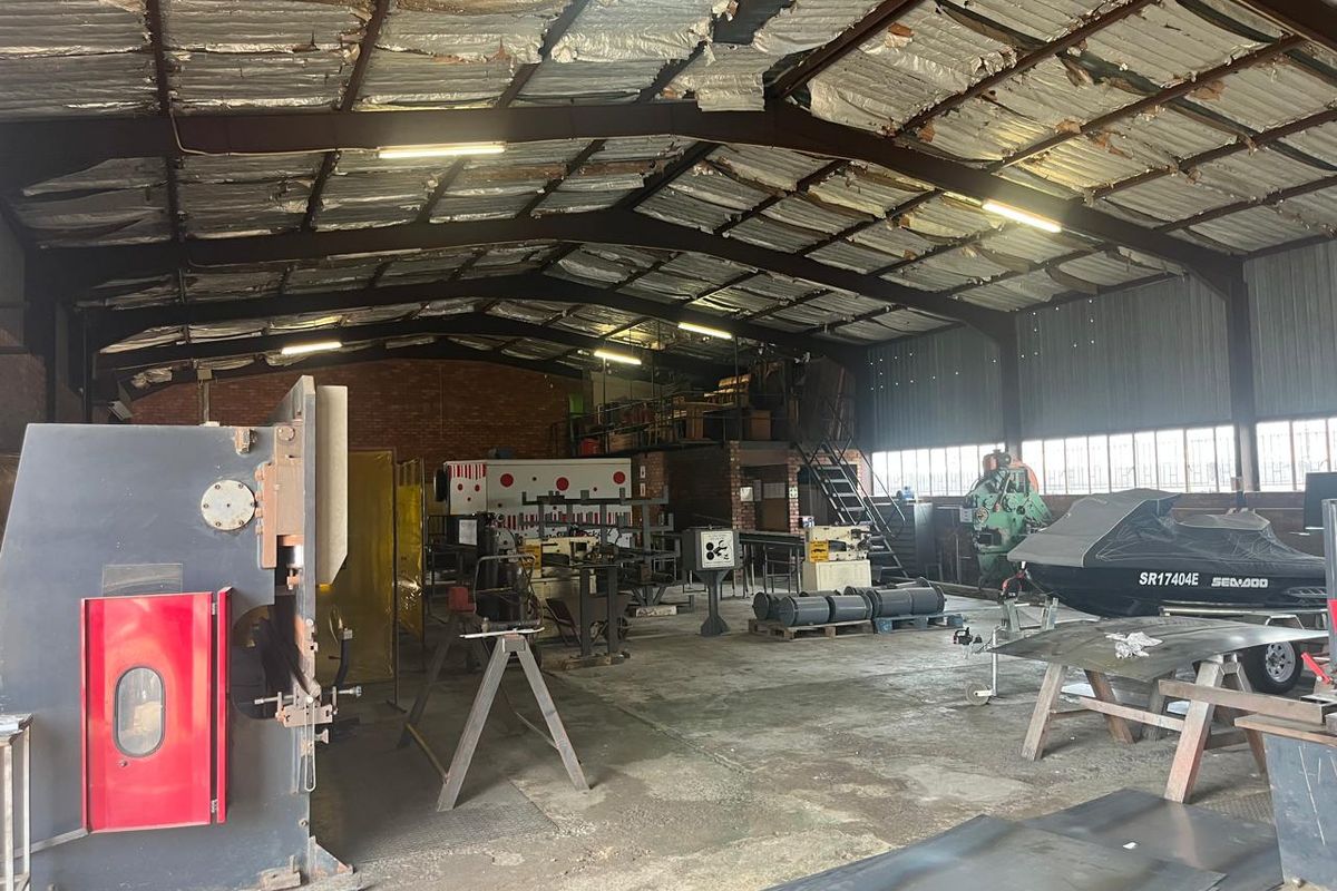 Spacious industrial workshop featuring exposed steel trusses, concrete flooring, a mezzanine level, and brick masonry walls, suitable for manufacturing or storage operations.