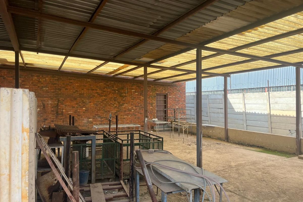 Covered outdoor utility or workshop area featuring a corrugated metal roof, steel structural supports, exposed brickwork, and a concrete perimeter wall.