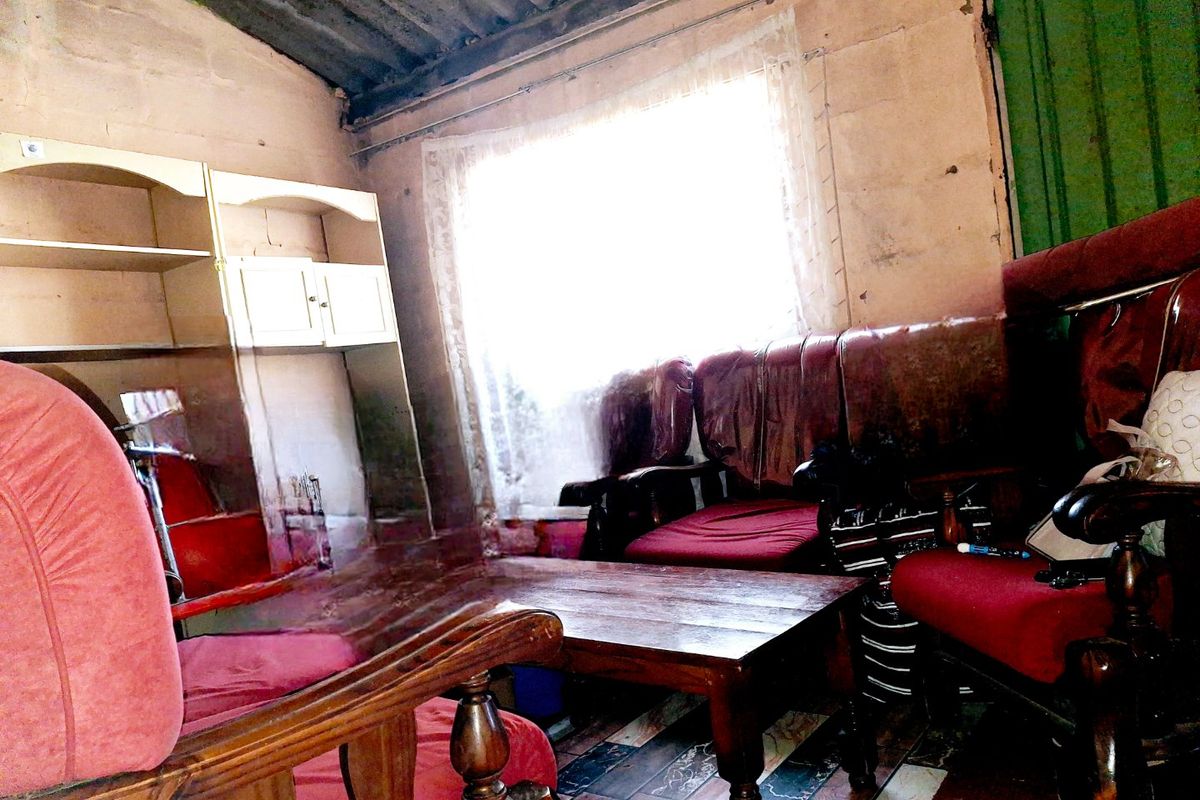A living room area featuring tiled flooring and an exposed corrugated iron ceiling, requiring significant renovation and cosmetic updates to improve the interior condition.