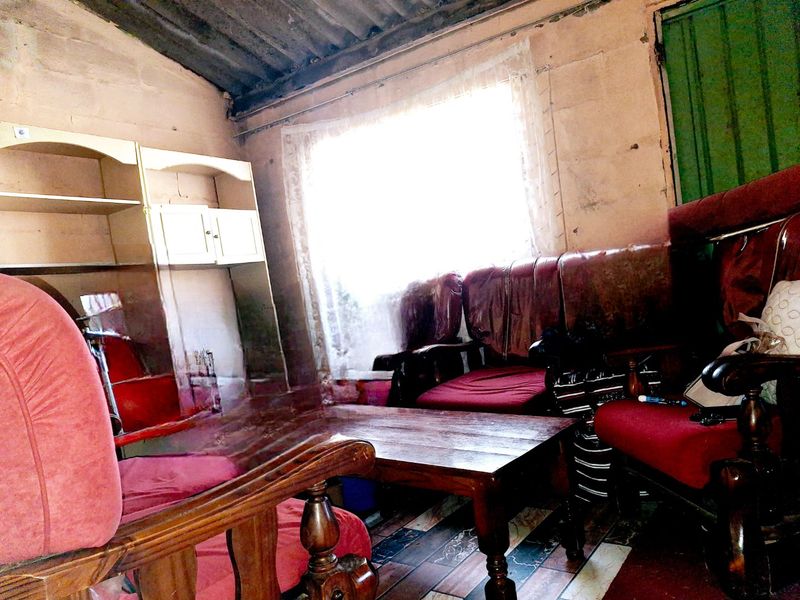 A living room area featuring tiled flooring and an exposed corrugated iron ceiling, requiring significant renovation and cosmetic updates to improve the interior condition.