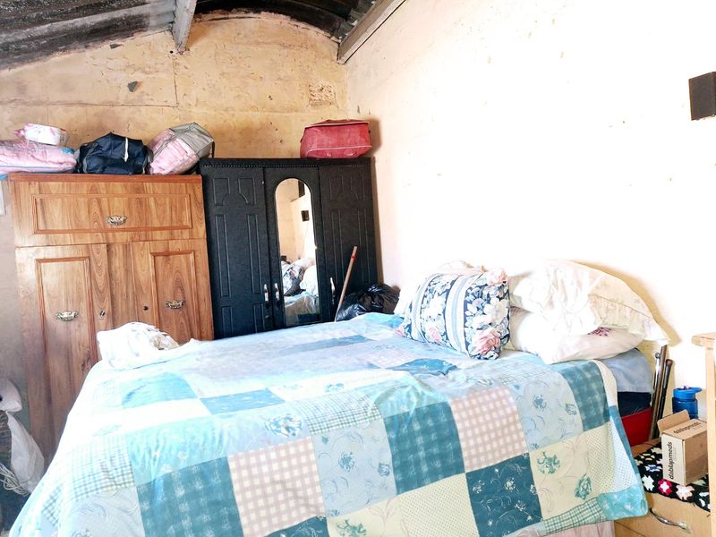 A bedroom featuring exposed roof rafters and unfinished masonry walls, requiring significant renovation and cosmetic updates to improve the living space.