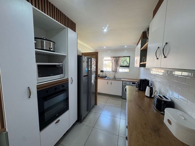 A functional kitchen featuring white cabinetry, wood-look countertops, subway tile backsplash, built-in oven, and microwave, with tiled flooring and recessed lighting.
