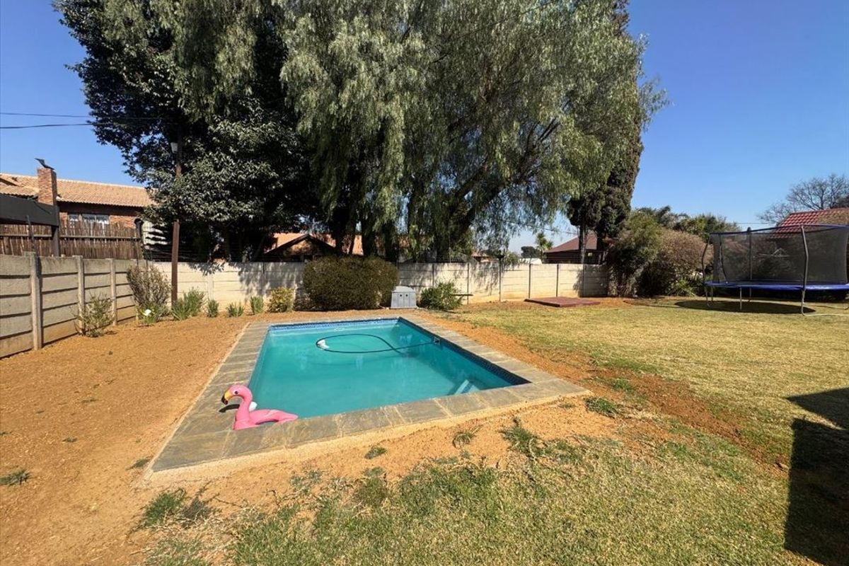 Outdoor pool area featuring a rectangular swimming pool with paved surround, set within a spacious garden enclosed by a precast concrete boundary wall.