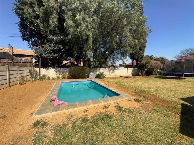 Outdoor pool area featuring a rectangular swimming pool with paved surround, set within a spacious garden enclosed by a precast concrete boundary wall.