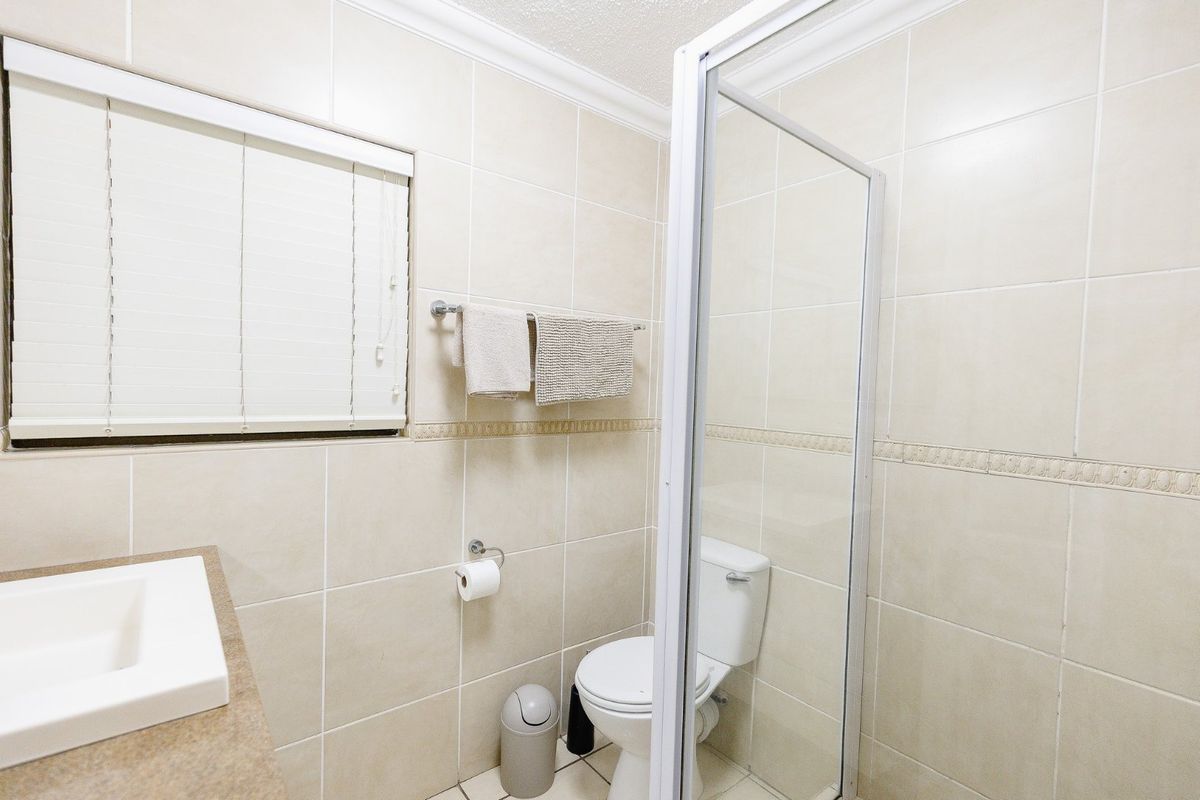 A clean, functional bathroom featuring a glass-enclosed shower, a wall-mounted vanity basin, and neutral floor-to-ceiling wall tiles.