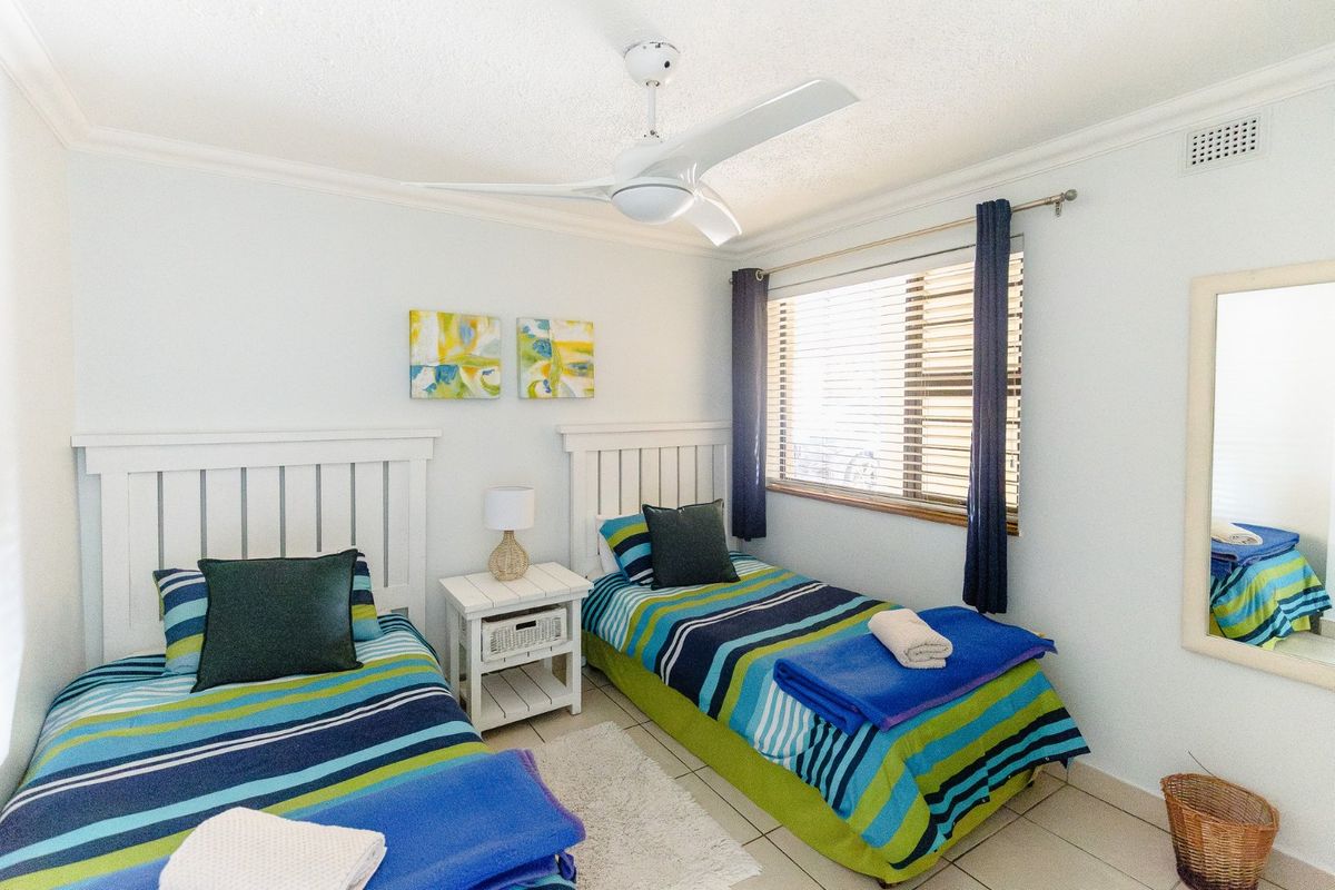 A functional twin bedroom featuring tiled flooring, a ceiling fan, and venetian blinds, providing a comfortable and well-lit sleeping space.