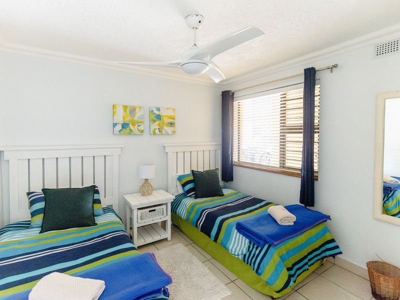 A functional twin bedroom featuring tiled flooring, a ceiling fan, and venetian blinds, providing a comfortable and well-lit sleeping space.