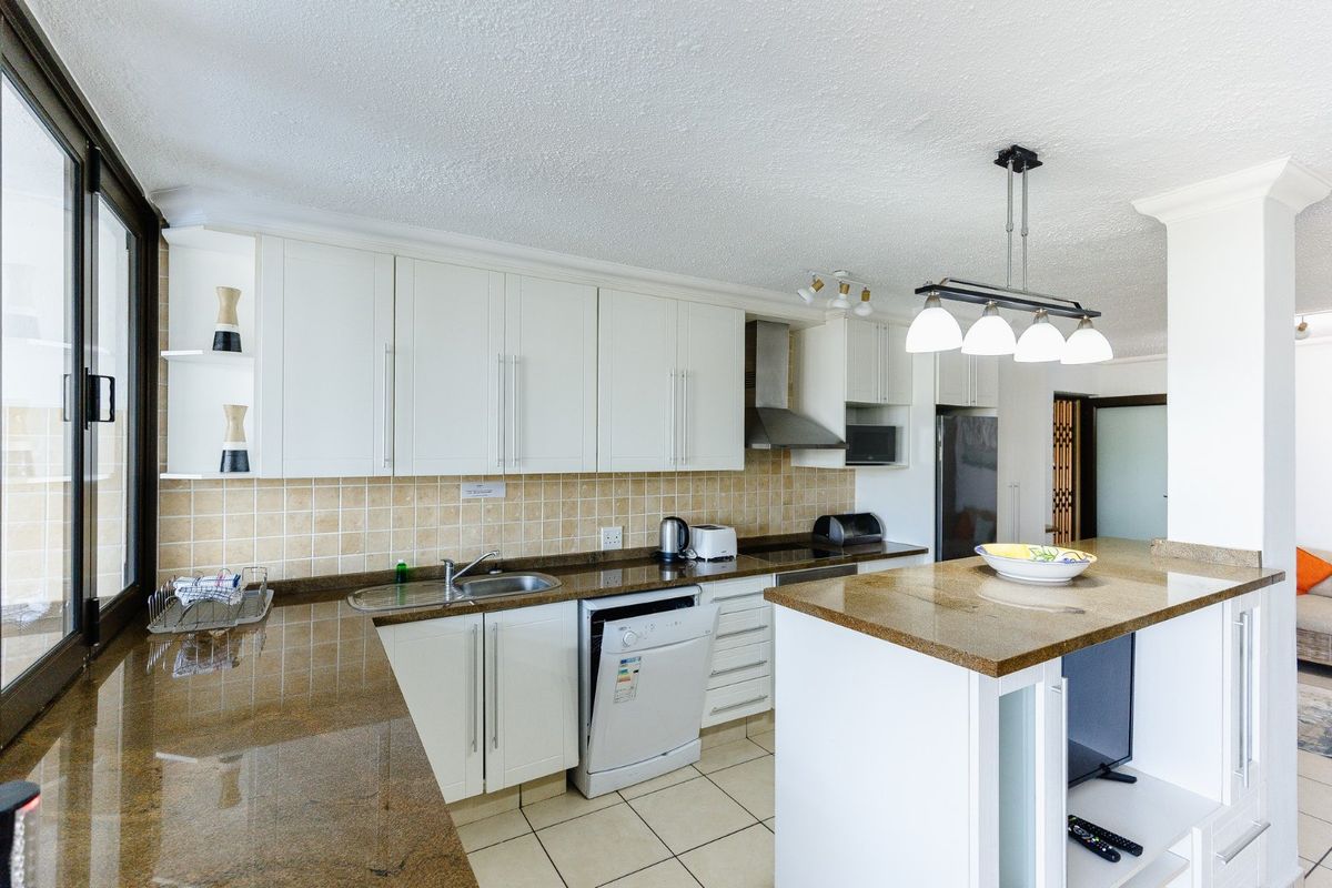 A functional kitchen featuring white cabinetry, granite countertops, a central island, and a tiled backsplash, offering a clean and practical workspace.