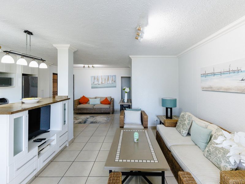 Spacious open-plan living and kitchen area featuring tiled flooring, a functional breakfast bar, and neutral finishes, offering a versatile layout for modern apartment living.