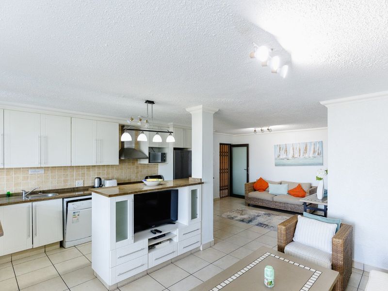 Open-plan living area featuring a functional kitchen with built-in cabinetry, tiled flooring, and a central island, seamlessly flowing into the adjacent lounge space.