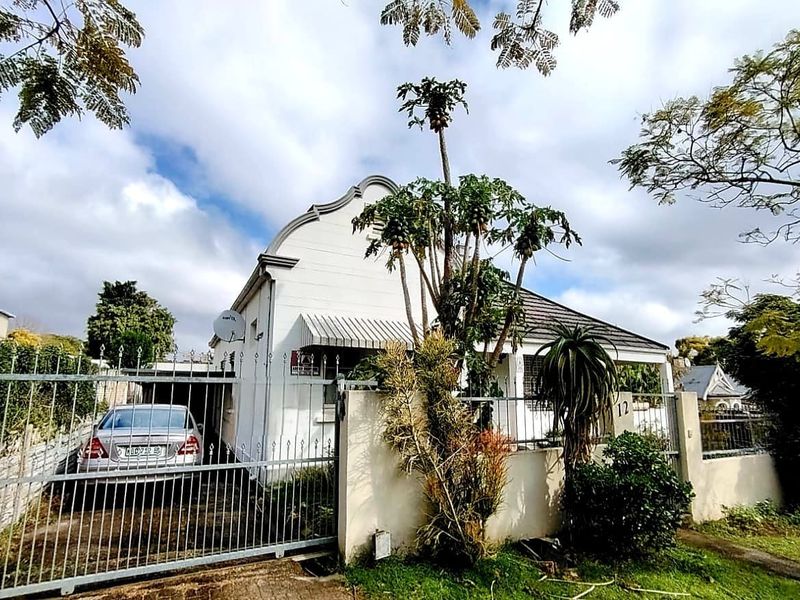 Front elevation of a residential house featuring a gabled roof, metal driveway gate, and perimeter walling with established garden elements.