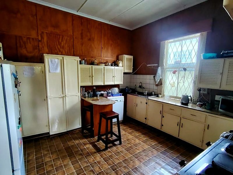 A dated kitchen featuring original cabinetry, tiled flooring, and wood-paneled walls, offering significant potential for a modern renovation and layout update.