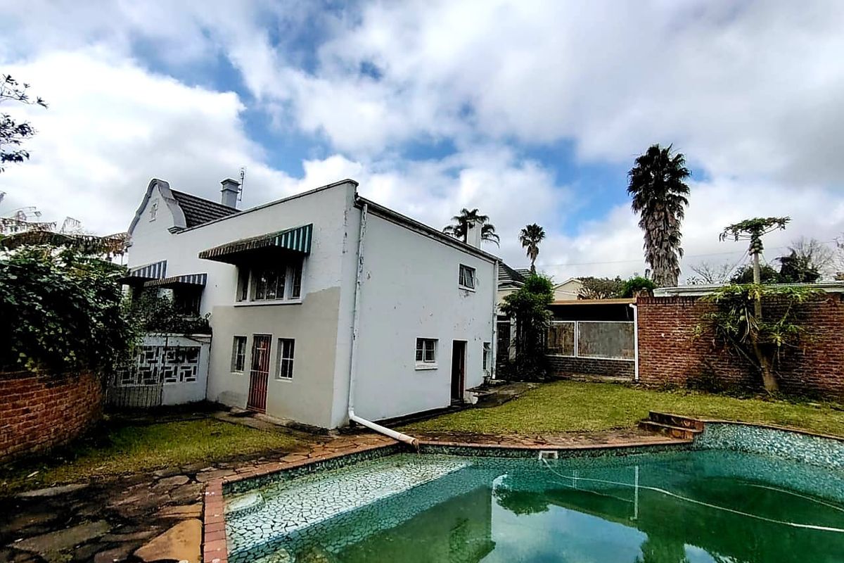 Rear exterior view of the property featuring a swimming pool, brick boundary walls, and a white facade with visible maintenance requirements.