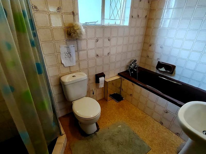 A dated bathroom featuring a bathtub, pedestal basin, and toilet with original wall tiling and worn flooring, offering potential for modernization.