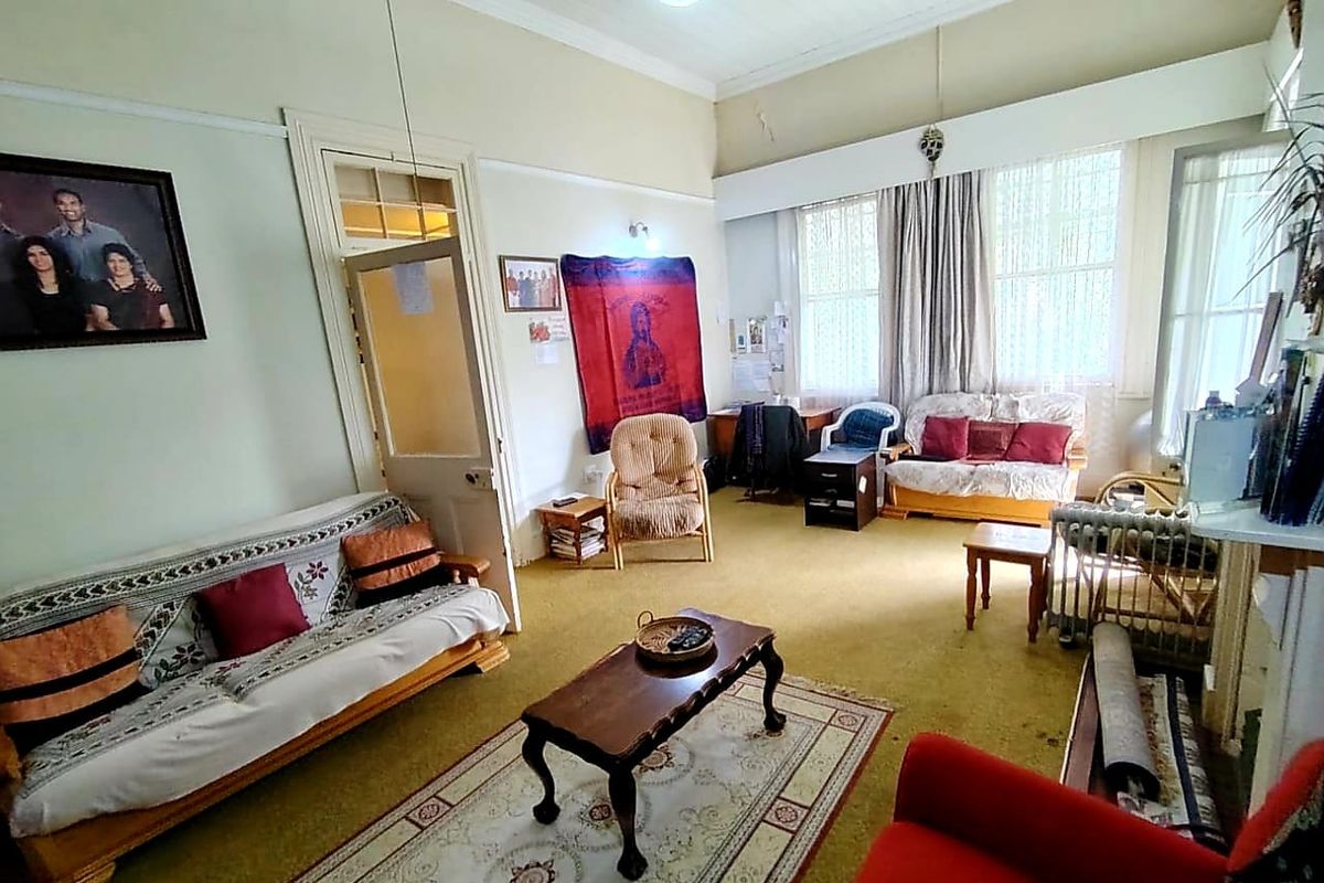 A spacious living room featuring high ceilings, traditional picture rails, and large windows that provide ample natural light.