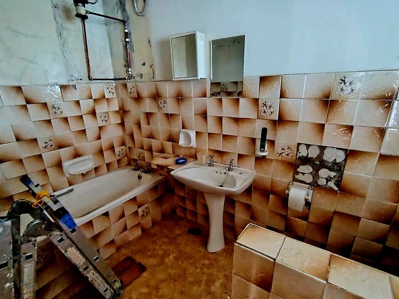 A dated bathroom featuring a pedestal sink and bathtub, currently undergoing renovation with visible wall damage and missing tiles.