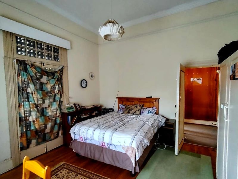 A bedroom featuring original hardwood flooring, high ceilings with decorative cornicing, and a classic transom window above the door.
