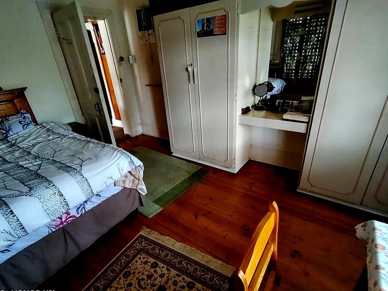 A bedroom featuring timber flooring and built-in wardrobe cabinetry with an integrated vanity area.