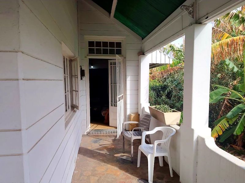 A covered veranda featuring timber weatherboard cladding, stone flooring, and a corrugated metal roof, providing a charming outdoor transition space.