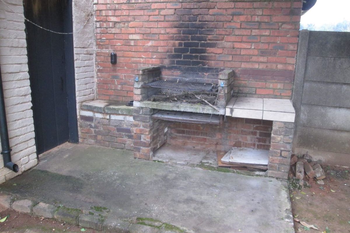 Outdoor rear area featuring a built-in brick braai and concrete patio, requiring maintenance and cosmetic updates to improve the entertainment space.