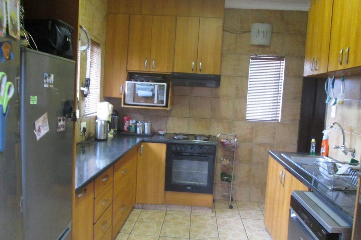 A functional kitchen featuring wooden cabinetry, granite countertops, built-in oven, hob, extractor fan, and tiled finishes throughout.
