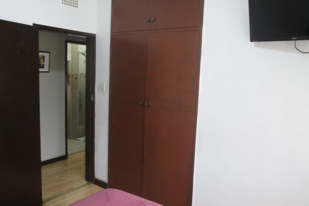 A bedroom featuring built-in wooden cupboards, laminate flooring, and a doorway leading to an adjacent bathroom.