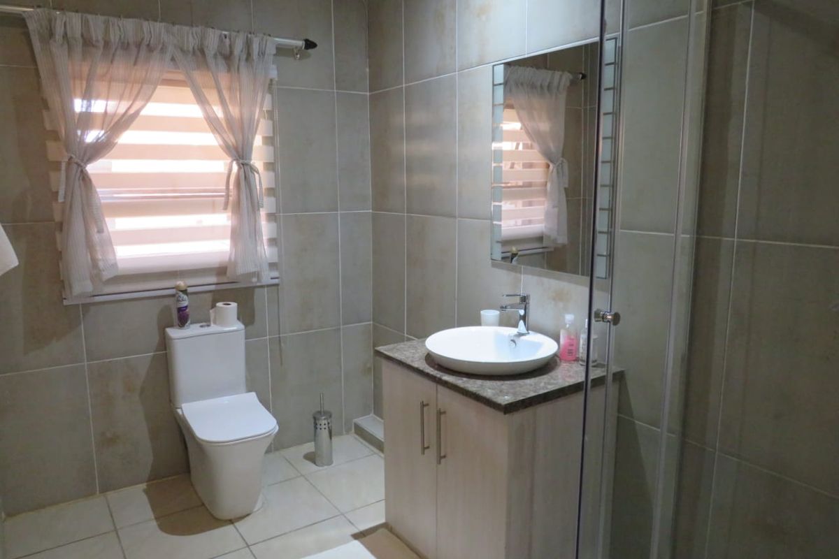 A well-maintained bathroom featuring neutral ceramic tiling, a modern vessel sink vanity, a toilet, and a glass-enclosed shower.