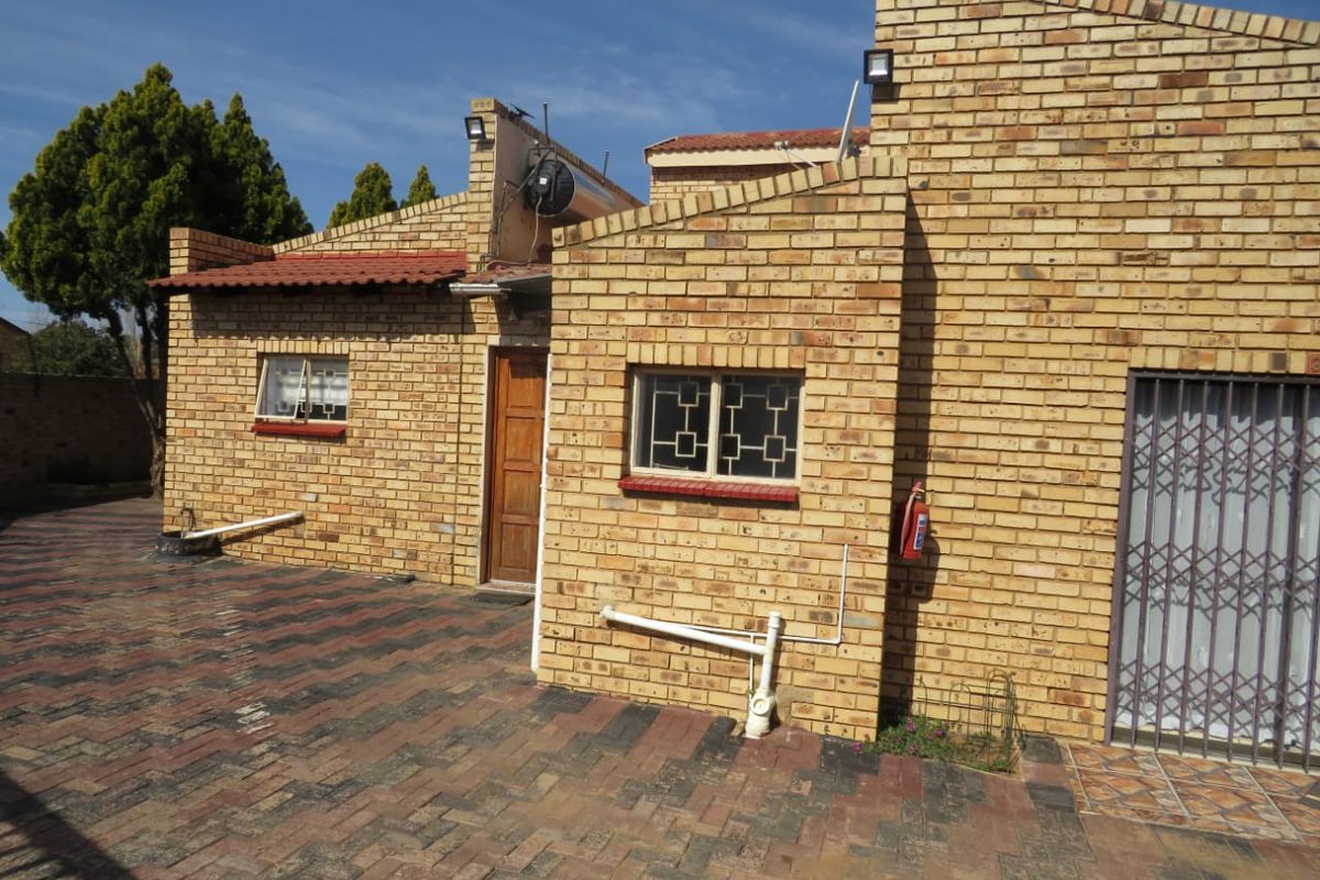 Rear exterior view of a face brick house featuring a paved courtyard, security gates, and external security lighting.