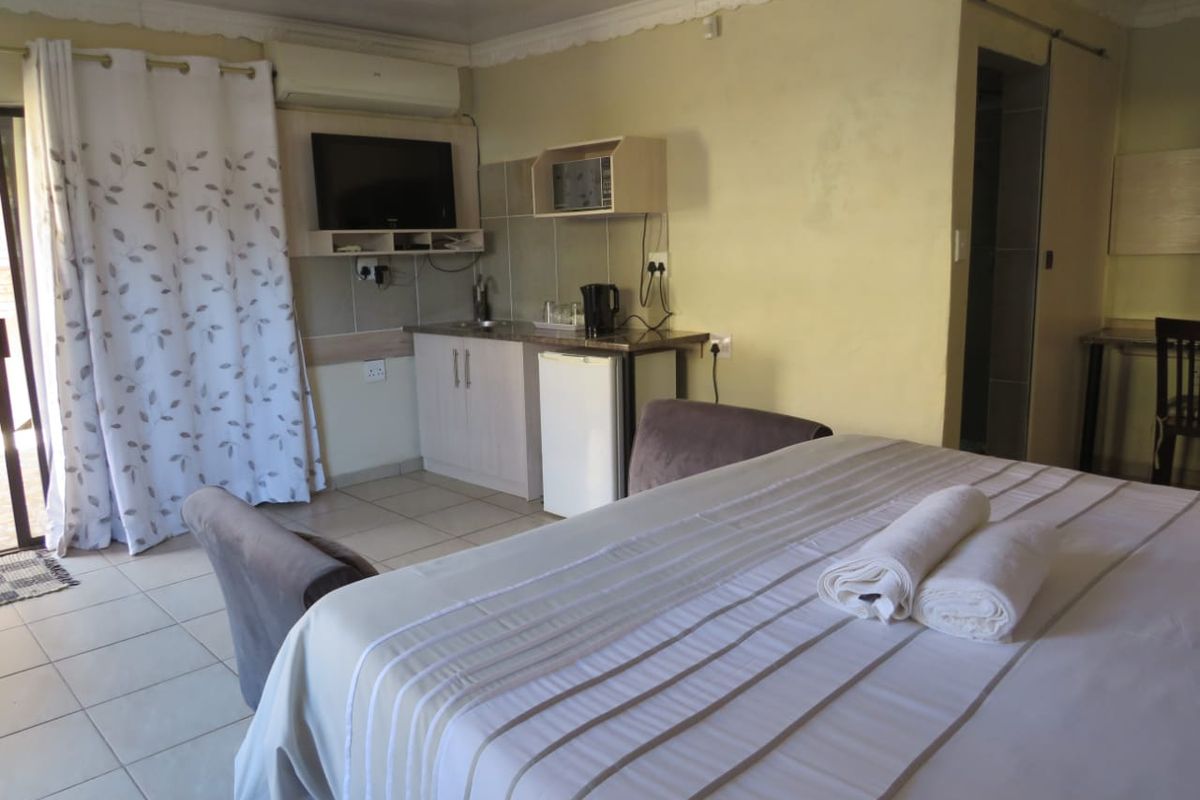 A bedroom featuring tiled flooring, crown molding, an air conditioning unit, and a compact kitchenette area with built-in cabinetry and a sink.
