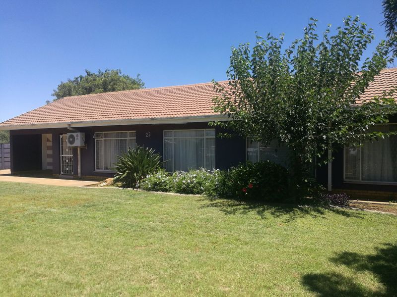 Front elevation of a single-story house featuring a tiled roof, established garden, and exterior air conditioning unit.