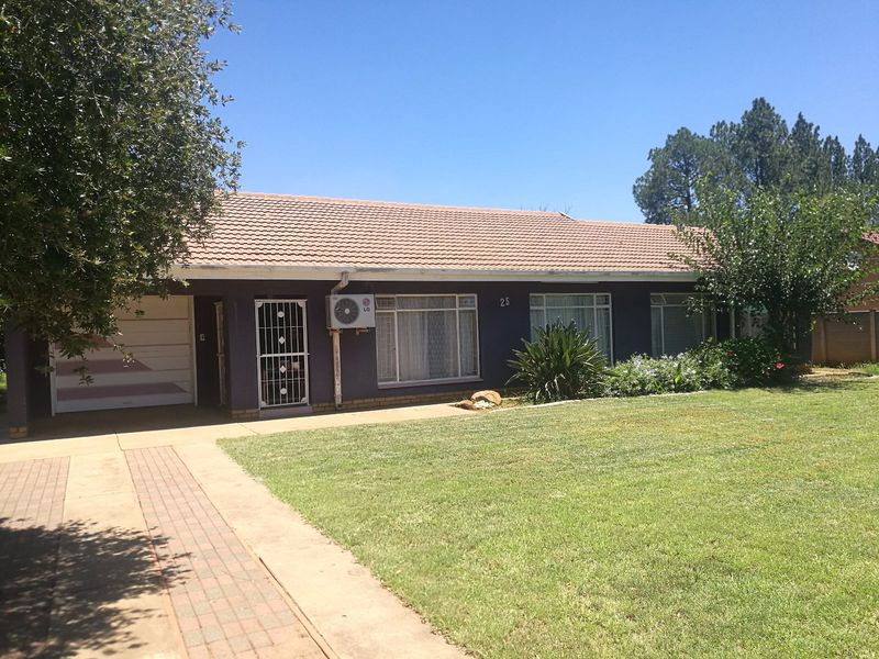 Front view of a single-story house featuring a tiled roof, paved driveway, attached garage, and a well-maintained front lawn.