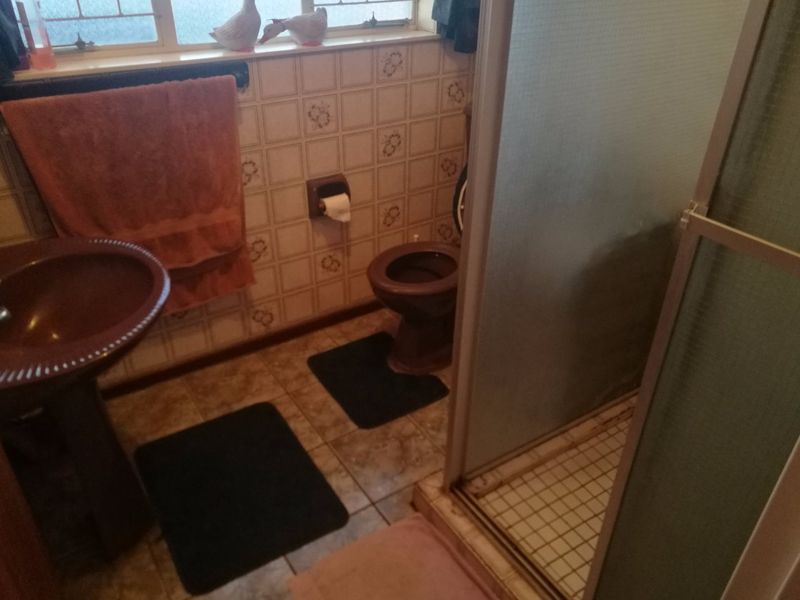 A dated bathroom featuring a pedestal basin, toilet, and shower enclosure with original wall and floor tiling.