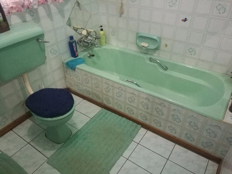 A dated bathroom featuring a vintage green bathtub and matching toilet, finished with patterned ceramic wall tiles and tiled flooring.