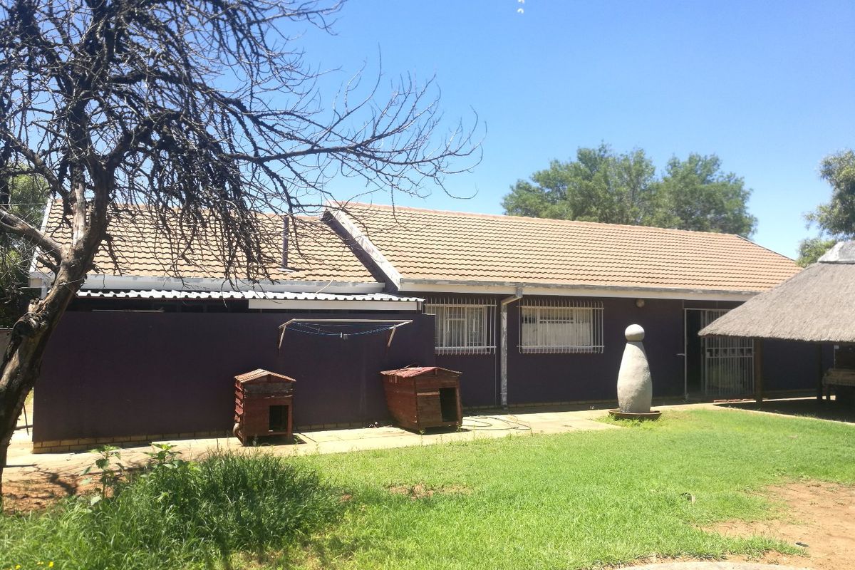 Rear view of the house featuring a tiled roof, security bars on windows, a paved patio area, and an adjacent thatched lapa structure.