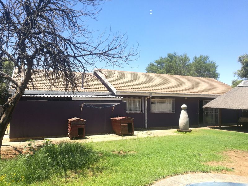 Rear view of the house featuring a tiled roof, security bars on windows, a paved patio area, and an adjacent thatched lapa structure.