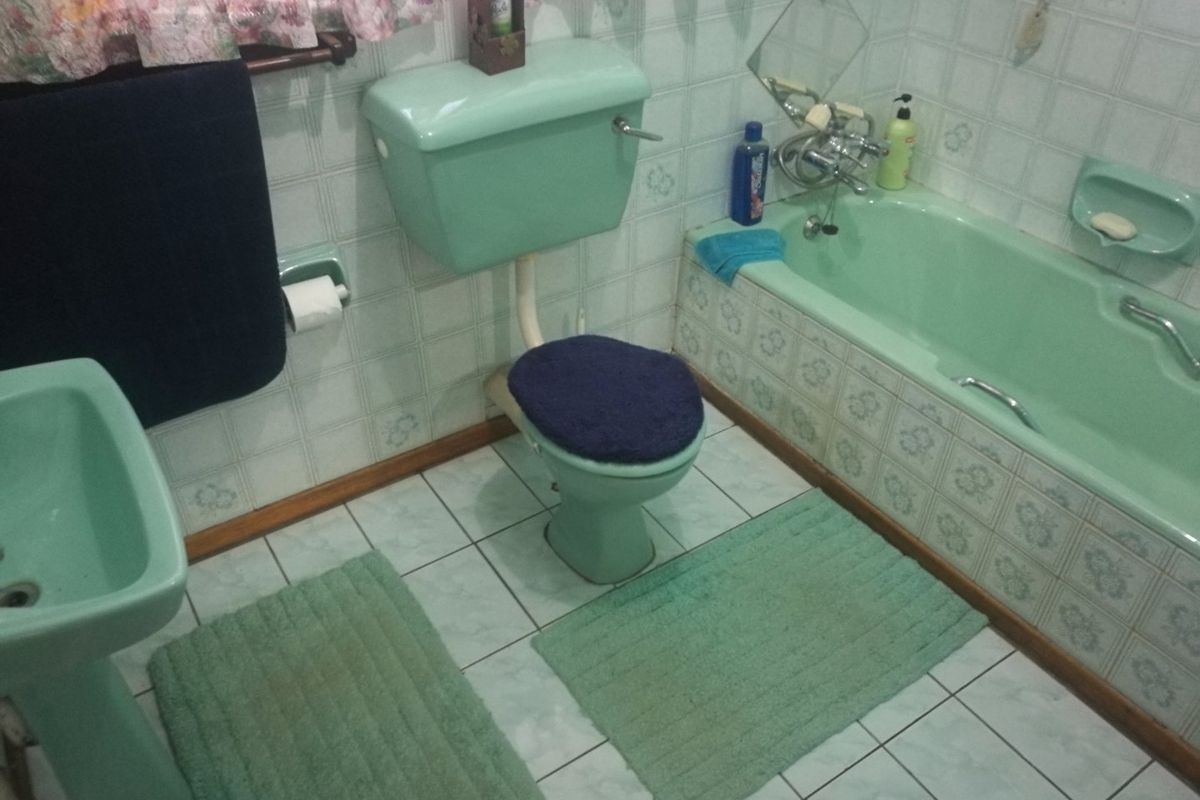 A dated bathroom featuring a vintage green suite including a pedestal basin, toilet, and bathtub with matching ceramic wall and floor tiling.