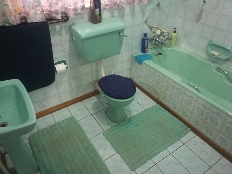 A dated bathroom featuring a vintage green suite including a pedestal basin, toilet, and bathtub with matching ceramic wall and floor tiling.