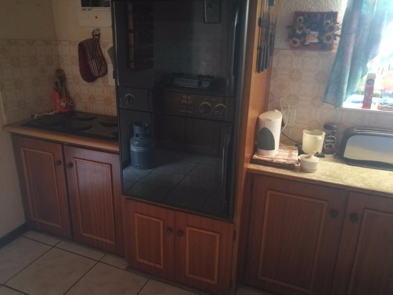 A dated kitchen featuring wooden cabinetry, tiled splashbacks, and built-in cooking appliances, offering potential for a modern renovation.