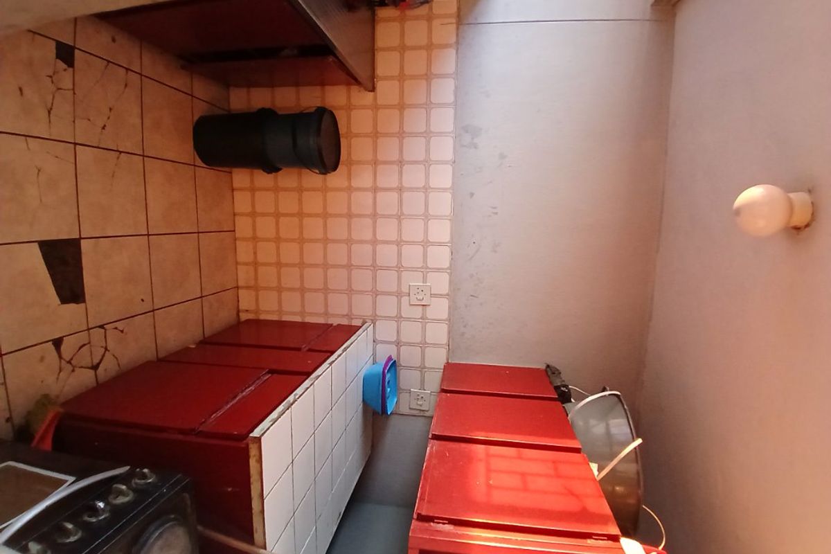 A dated kitchen area featuring tiled countertops, built-in cabinetry, and a stove, requiring significant cosmetic updates and repairs to the flooring and wall finishes.